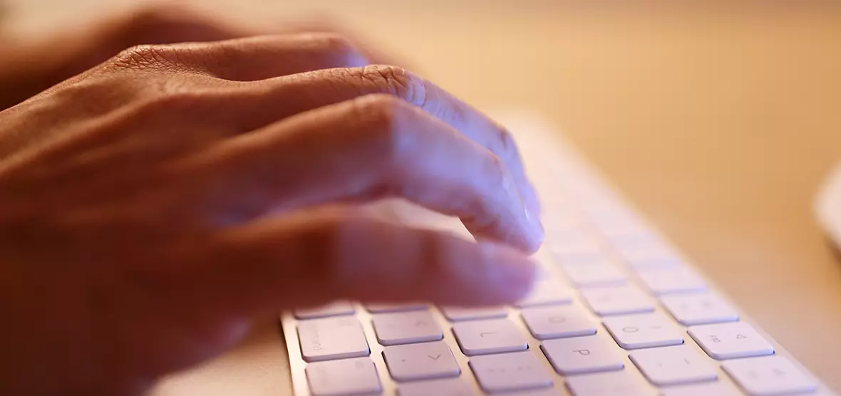 A close up of hands typing on a white keyboard