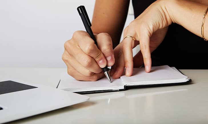 Female hands write pen in a notebook of tasks and goals to work on a wooden table.