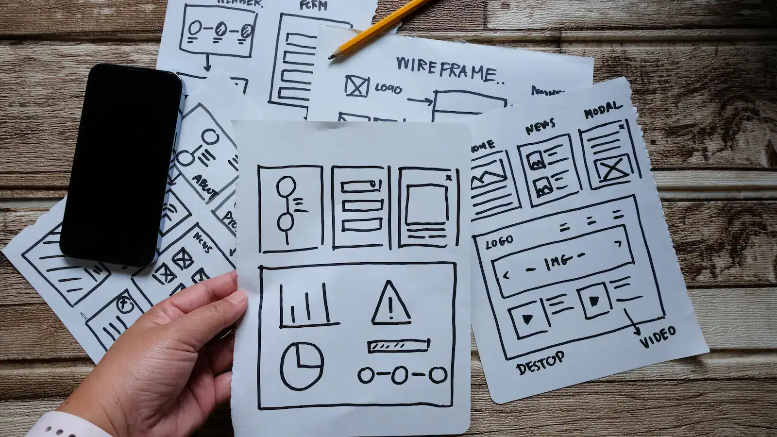 Hand holding website wireframe sketches on desk